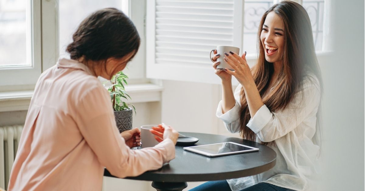 Chicas divertidas sentadas alrededor de una mesa redonda con un te