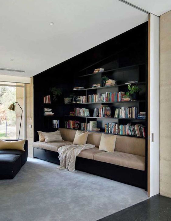 Soul-espacios-0_10B BIBLIOTECA Habitación con pared de baldas para libros en color oscuro y bancada de asiento en la parte delantera